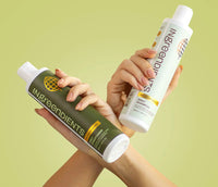 A person holding both Daily Shampoo and Conditioner by Ingreendients in criss-crossed arms.