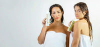 Two women wrapped in white towels, holding Ingreendients daily shampoo and volumizing shampoo bottles.