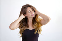 A young woman with long, brown, wavy hair, massaging her scalp with her hands.