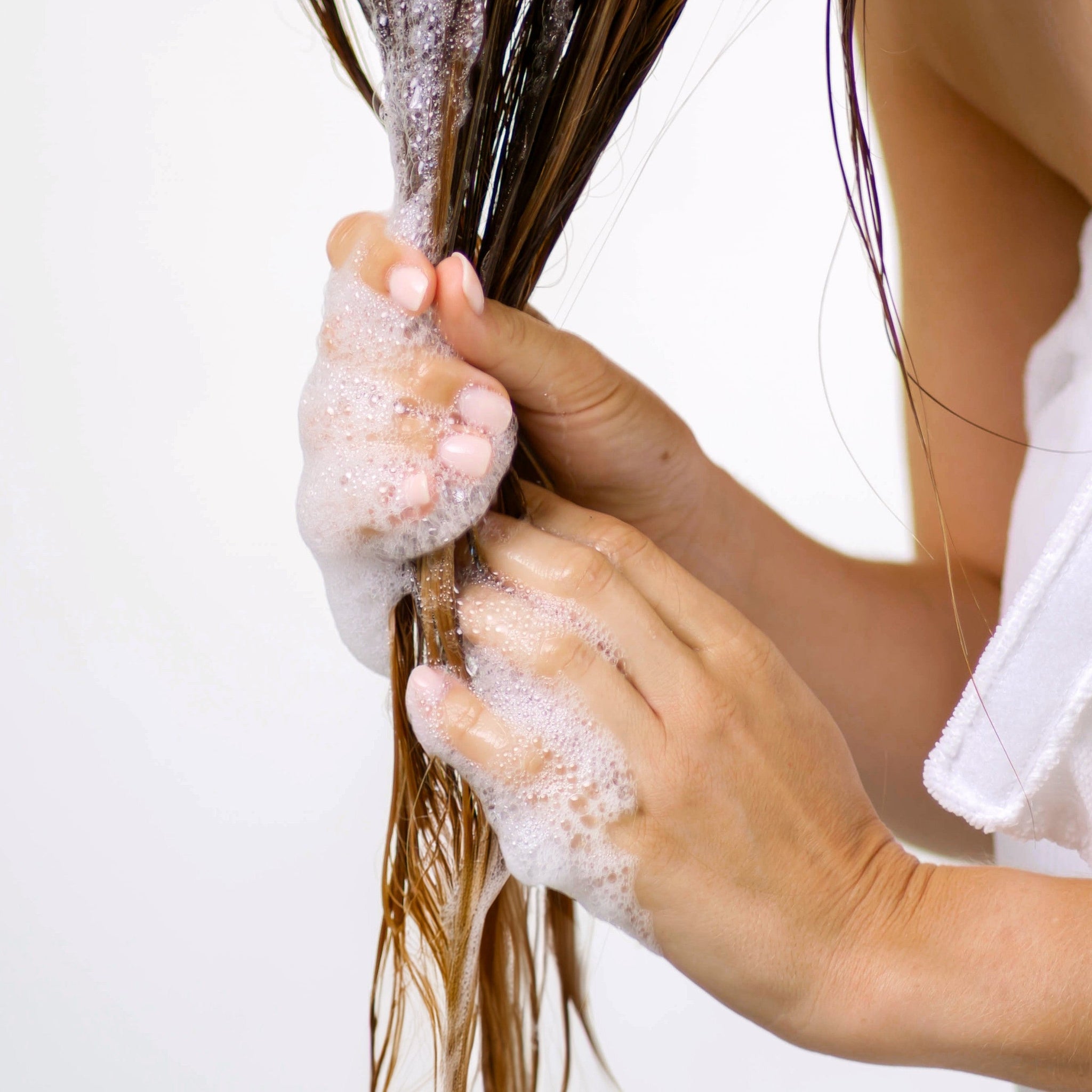 Close-up of wet, long brown hair being gently squeezed by hands with Ingreendients’ shampoo lather running down.